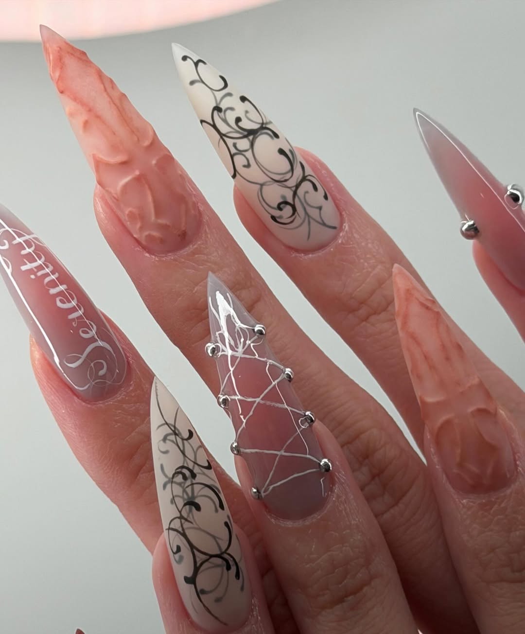Ethereal Serenity Nude and Gray Stiletto Nails with Baroque Script and 3D Cross Design